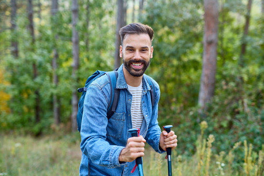 Hiking man enjoys nature with trekking poles in a lush forest during a sunny day