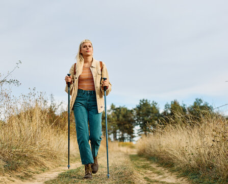 Hiking woman enjoys nature with trekking poles in a lush forest during a sunny day
