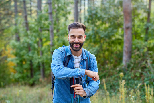 Hiking man enjoys nature with trekking poles in a lush forest during a sunny day