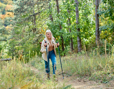 Hiking woman enjoys nature with trekking poles in a lush forest during a sunny day