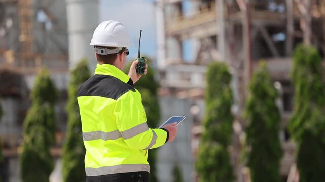 Industrial engineer in high visibility vest communicating with radio at construction site, Worker man monitoring refinery infrastructure, Technician checking equipment at oil and gas production plant
