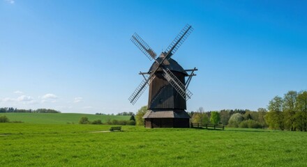 Naklejka premium A tall, wooden windmill stands in a vibrant green field under a clear blue sky