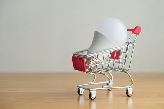 Electric light bulb in shopping trolley on wooden table with white wall background. Find the best deal and choose the electricity plan from supplier to shop electricity for home or business concept.
