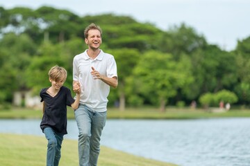 Fototapeta premium Smiling Father and Son Running Together in Park Enjoying Wellness Lifestyle and Healthy Outdoor Activity. Happy Parent and child Jogging Along Lakeside joyful emotional bonding family moment