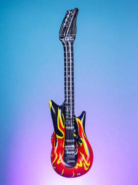 Close-up of a blow-up toy shaped like a guitar on a purple background, highlighting its bright colors and playful design
