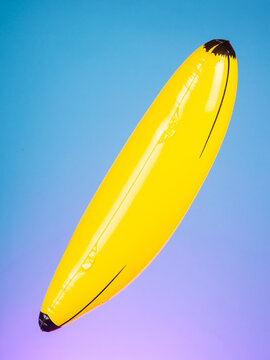 Close-up of an inflatable yellow banana toy on a purple background, highlighting its bright color and playful design