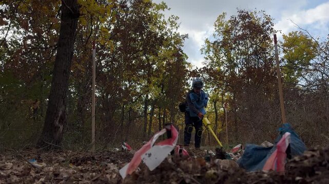 Mykolaiv, Ukraine &ndash; October 20, 2024 &ndash; A humanitarian deminer in protective gear sweeps the autumn forest floor with a handheld mine detector during clearance operations