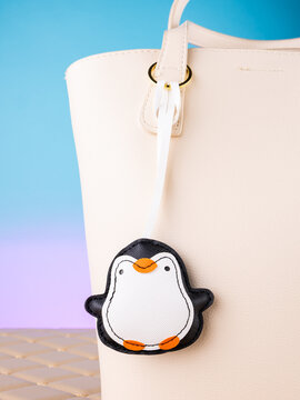 Close-up of a leather bag charm with a cute penguin, on a  white bag. Elegant and charming accessory