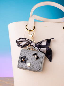 Close-up of a leather mini bag-shaped keychain with bow and charmson a  white bag. Elegant and charming accessory.