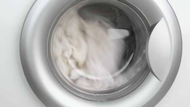 Close-up of a hand opening the hatch of a washing machine. Washed clothes are visible inside.