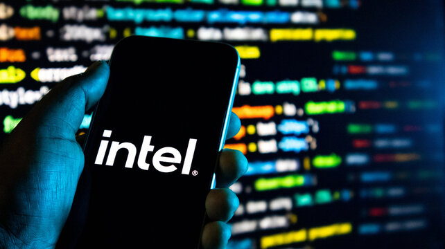 Hand holding a smartphone with the intel logo on the screen against a background of computer code