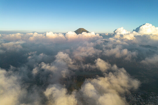 Aerial view of a volcanic mountain peak rising above a thick layer of clouds during golden hour in Indonesia.