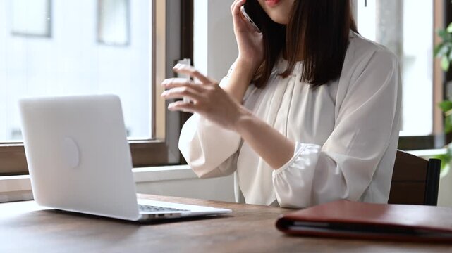 スマートフォンで通話をしながらノートパソコンで仕事をする女性