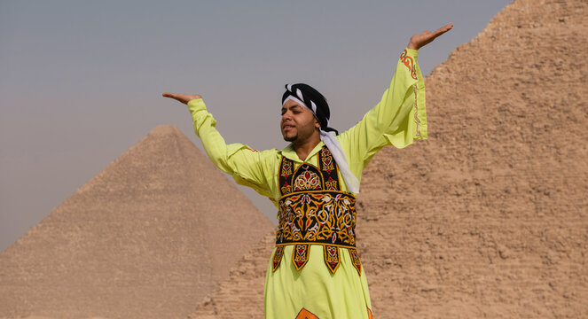 Egyptian folk dancer wearing vivid lime green embroidered galabiya and headwrap spreads arms in joyful expressive pose before ancient pyramids ideal