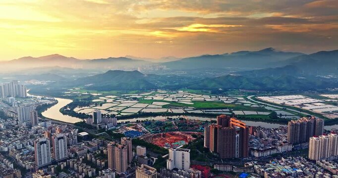 Aerial view of a modern city skyline and river with traditional fish ponds at golden sunset in Shenzhen, China