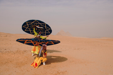 Fototapeta premium Two tanoura dance performers in vivid embroidered costumes fan spinning skirts dramatically before pyramid silhouettes in open Egyptian desert ideal