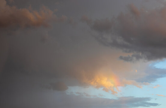 Dramatic sunset sky with colorful clouds and a subtle rainbow fragment appearing after rain