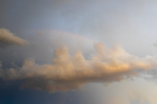 Golden cumulus cloud in the evening sky with subtle rainbow iridescence and pastel colors