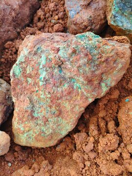High grade nickel ore specimen with green garnierite minerals in red laterite soil. Mining industry, exploration, and energy resource concept