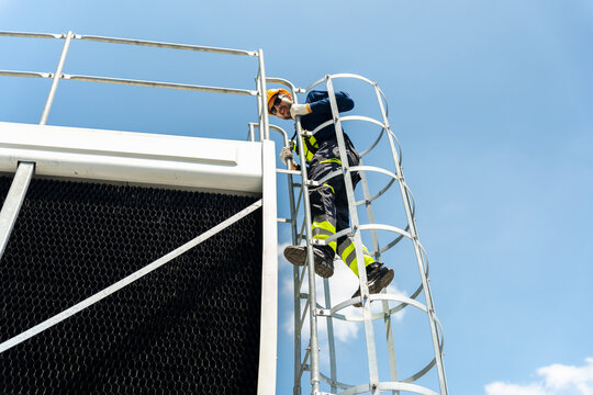 Technician man climbing a safety ladder to inspect industrial cooling system, Industrial maintenance worker in safety gear climbing a caged ladder, Professional worker accessing HVAC equipment