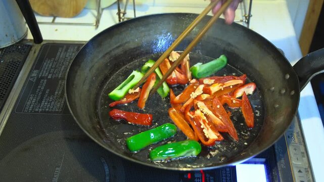 大型直径32cmの鉄フライパンを用い、肉野菜炒めの調理で、緑ピーマンと赤ピーマンを炒めているシーン　59秒