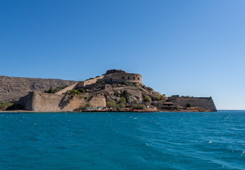 Obraz premium Ancient Venetian fortress on Spinalonga Island rises directly from turquoise sea water under clear blue sky near Crete coast.
