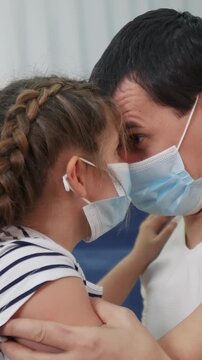 A man and a girl are close together, sharing an intimate moment while wearing face masks. The man and the girl display a connection in a private setting.