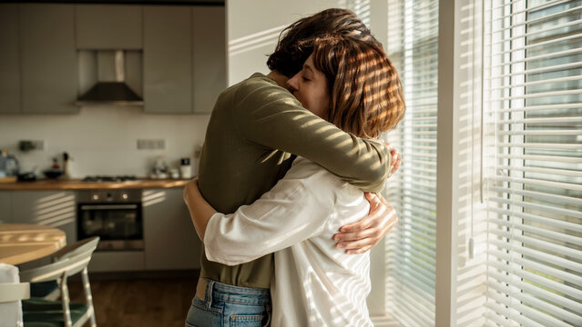 Couple embracing warmly in kitchen by window for love support and intimate home relationship