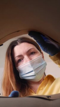 A woman wearing a mask inspects an opening, focused on her task. Her gloves and mask indicate a careful approach in this possibly medical or cleaning setting.