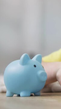 A blue piggy bank sits on a table. A child's hand reaches toward the blue piggy bank, indicating interest in savings.