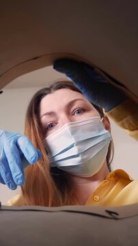 A woman wearing a mask inspects something closely, focusing intently on her task. She uses gloves to touch the object while ensuring safety during the inspection.