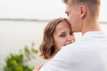 Fototapeta premium Young couple sharing a tender moment with a forehead kiss by the water