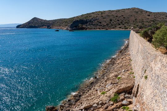 Long historic stone fortress wall by blue sea on Spinalonga island Greece