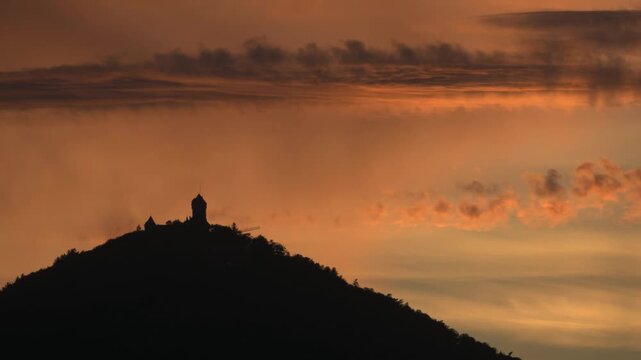 Silhouette of Haut Koenigsbourg castle at sunset. Orange clouds scroll by in timelapse.
