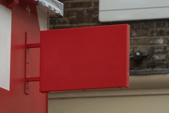 Blank red projecting storefront sign mockup on urban building exterior