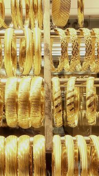 Close-up of ornate gold bangles and bracelets displayed on metal rods in a jewelry shop, with shimmering reflections and slight camera movement across the collection