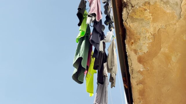 Colorful clothes dry on a clothesline hanging from an old balcony in Simferopol, Crimea. This simple everyday view against the clear blue sky brings a cozy, nostalgic, and peaceful feeling.