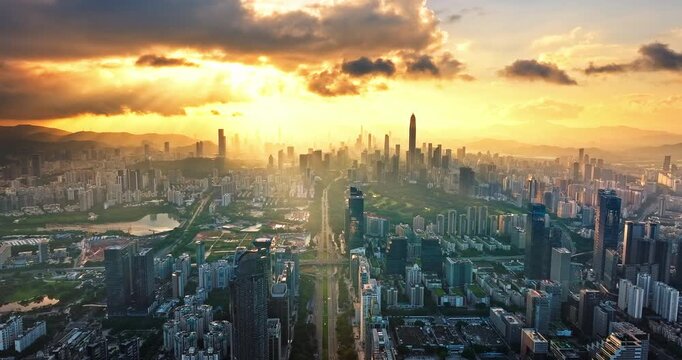 Panoramic drone view of Shenzhen city skyline at golden sunrise with sun rays shining through clouds, Guangdong, China