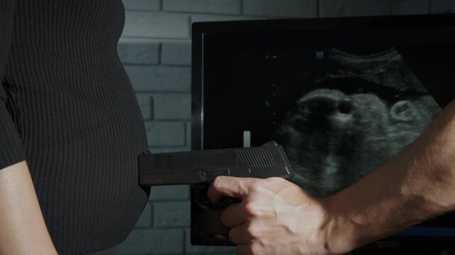 Unhealthy pregnancy time. View of gun by pregnant belly. A concept of health problems and abortion in woman's life