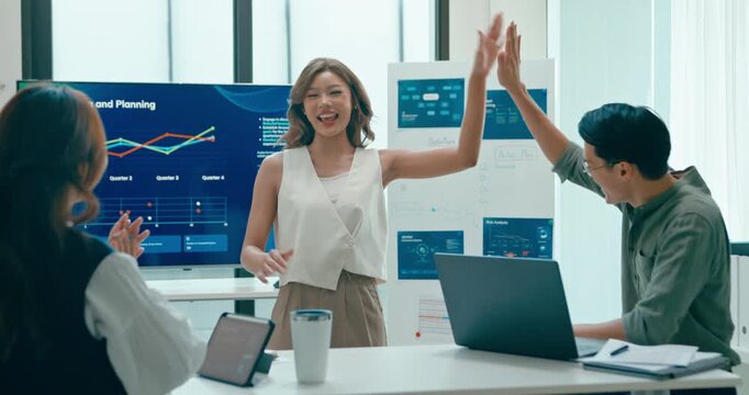 Group of Asian businesspeople work together leads business meeting uses presentation TV with revenue, profit or sale statistics in office. Financial generation z team brainstorm on e-Commerce project.