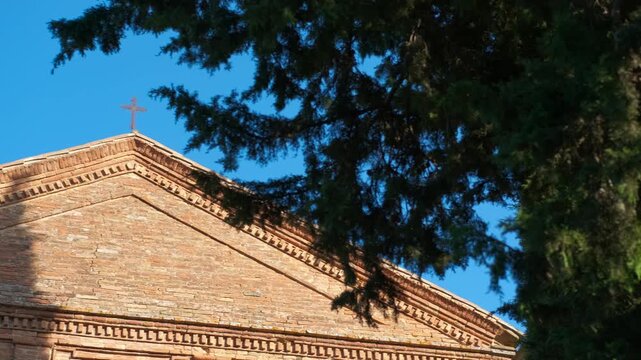 Church facade pediment with a christian cross revealing. Revealing shot of an ancient brick church facade with a pediment, a christian cross on the top of the roof, against a clear blue sky
