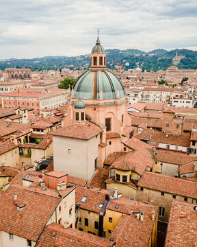 Aerial view of the historic cathedral dome rising above the dense terracotta rooftops of the city center in Bologna, Emilia-Romagna, Italy.