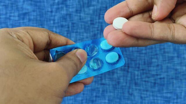 Hands pushing on medicine cover and take out pill or tablet from inside the blister pack. Concept of daily dosage of medication, pharmaceutical industry, health care treatment or vitamin supplement.