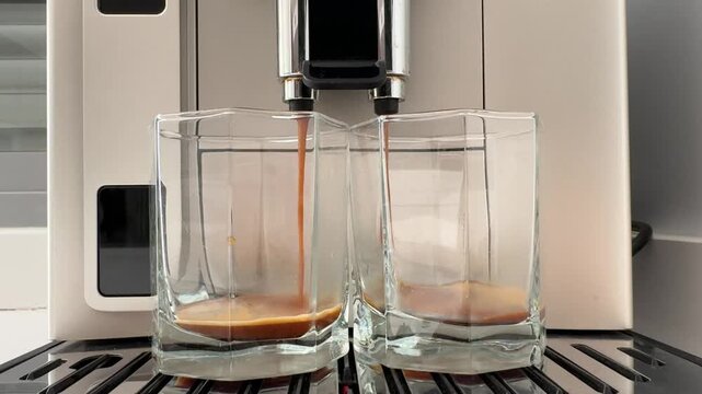 Espresso pours into two clear glasses on the drip tray. Fresh double shot brewing at home