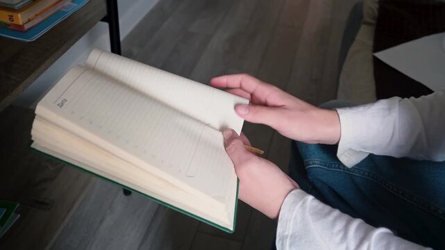 Close-up of Young Person Hands Holding and Flipping Pages of Blank Lined Notebook or Planner