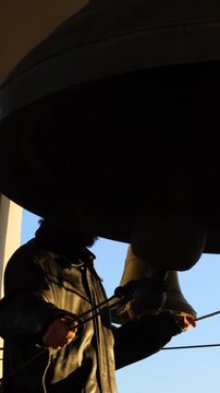 Street musician plays violin beneath balloon canopy, silhouetted against blue sky, bow moving across strings as hands hold instrument in warm sunset light, posture steady, violin angled upward.