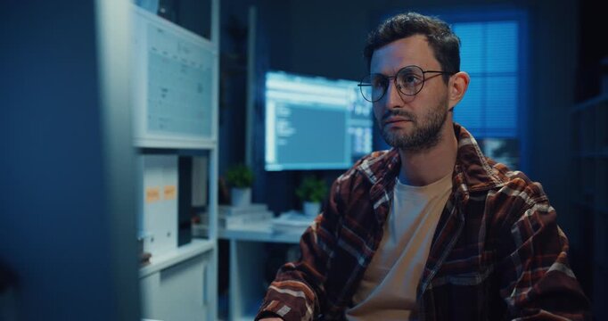 Young Caucasian male programmer write code on computer in home office at late night. AI technology, cybersecurity, software developer, freelance innovation, database system, digital network concept.