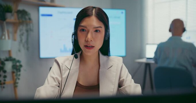 Young Asian female agent talking on phone headset consulting client online in call center office. Corporate customer service, technical support, remote tech operator, business team help desk concept.