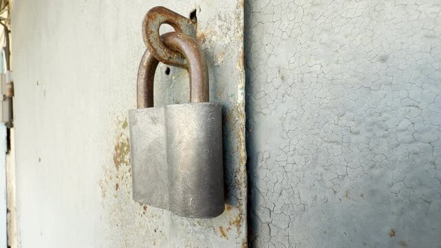 A rusted padlock hangs securely from a weathered metal door. This forgotten object feels lonely and protective, guarding a mysterious entrance in the quiet light.