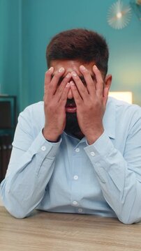 Indian man at home buries face in palms fatigued by burnout stress hopeless after brutal day. Arabian guy at desk shakes quietly feeling deep despair seeking relief from pressure and mental overload.